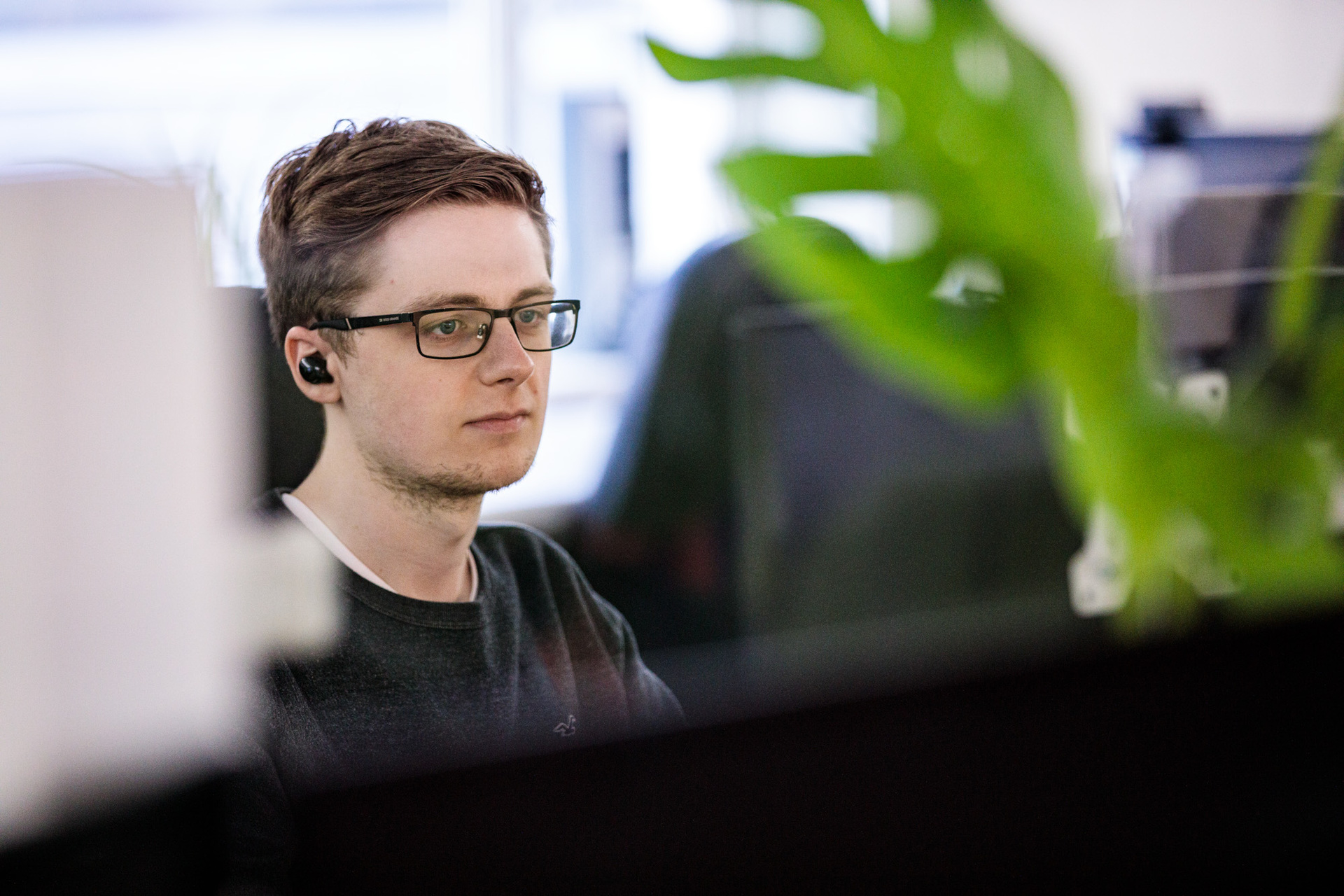 A male web designer with earphones in staring at his desktop computer